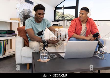 Enregistrement de divers amis masculins assis sur le canapé dans le home studio, avec ordinateur portable et microphones Banque D'Images