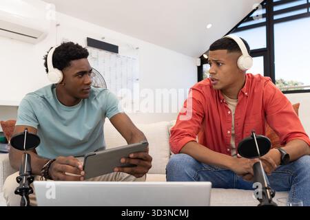 Enregistrement de divers co-hôtes masculins parlant dans des microphones dans le studio loft, avec ordinateur portable et tablette Banque D'Images