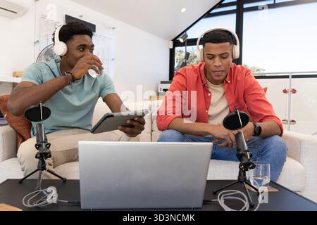 Enregistrement de divers amis masculins assis dans le home studio, en utilisant des écouteurs, ordinateur portable et microphones Banque D'Images