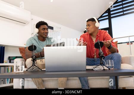 Enregistrement de divers co-animateurs masculins discutant de podcast dans le bureau à domicile, avec des microphones et un ordinateur portable Banque D'Images