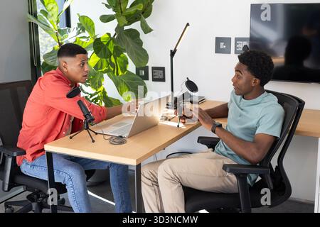 Discuter de divers collègues masculins travaillant ensemble au bureau du studio, avec des microphones et un ordinateur portable Banque D'Images