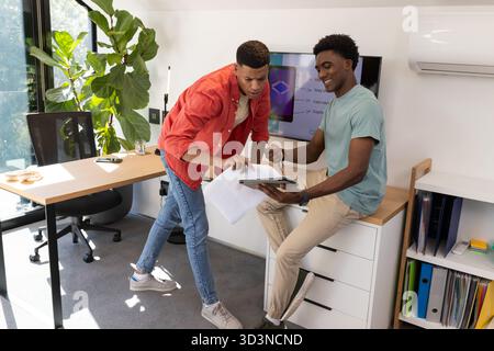 Collaboration de divers collègues masculins examinant des documents au bureau dans le bureau avec tablette, tasse à café Banque D'Images