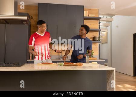 Saupoudrer de fromage, divers amis masculins préparant des bases de pizza sur l'île de marbre avec de la sauce, des herbes Banque D'Images