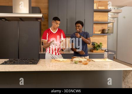 Préparer des croûtes de pizza divers amis masculins cuisinant à l'îlot de cuisine en marbre, avec des garnitures de pizza Banque D'Images