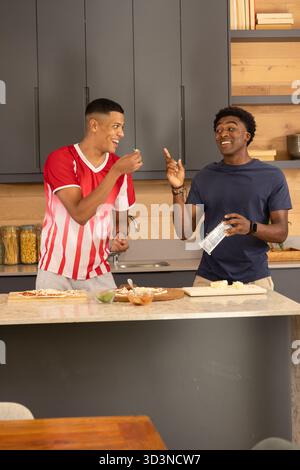 Préparer divers amis masculins assemblant des pizzas sur l'île de marbre dans la cuisine, avec de la sauce et du fromage Banque D'Images