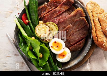 Steak de porc grillé avec salade verte et légumes dans une assiette sur un fond clair. Vue de dessus. Banque D'Images