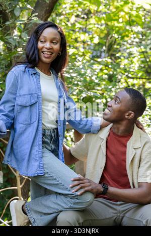 Équilibre couple afro-américain sur la racine d'arbre dans le sentier forestier, avec smartwatch sur le poignet de l'homme Banque D'Images