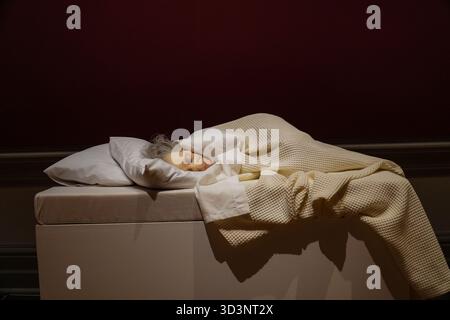 La sculpture hyperréaliste de Ron Mueck, 'Old Woman in Bed', montre une femme âgée aux cheveux gris dormant paisiblement sous une couverture beige en tricot gaufré, Banque D'Images