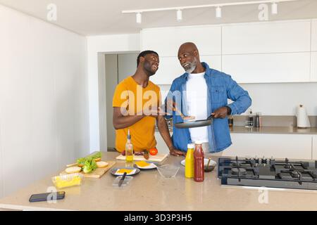 Cuisine afro-américaine père et fils préparant des hamburgers à l'îlot de cuisine moderne, avec poêle à frire Banque D'Images