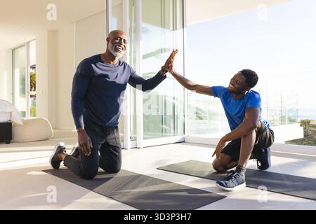 Père et fils afro-américains chevronnés agenouillés sur des tapis de yoga dans la salle de gym à domicile avec des baskets Banque D'Images