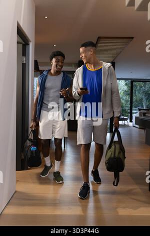 Marcher divers amis masculins transportant des sacs marins dans le couloir de la maison moderne, avec smartphone Banque D'Images