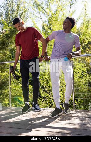 Penchant divers amis masculins discutant contre la balustrade en métal sur le pont en bois, avec des bouteilles d'eau Banque D'Images