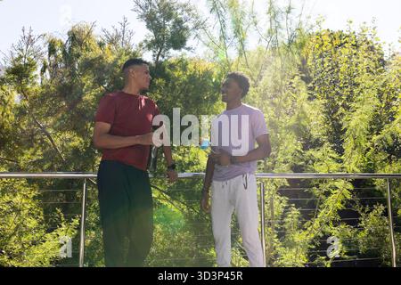 Bavarder divers amis masculins debout sur le pont dans le parc, avec des bouteilles d'eau et de la rampe Banque D'Images