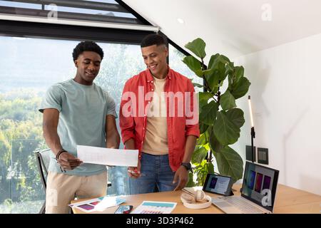 Examen de divers collègues analysant des documents de conception au bureau à domicile, avec des diagrammes de couleurs et un ordinateur portable Banque D'Images