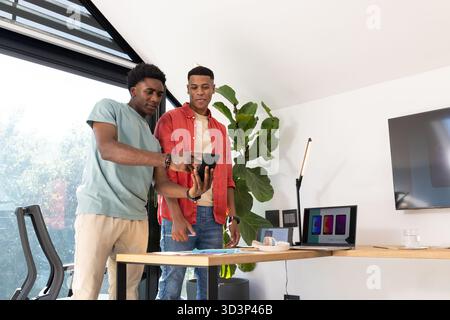 Penchant divers collègues masculins examinant des maquettes de conception au bureau, avec smartphone et ordinateur portable Banque D'Images