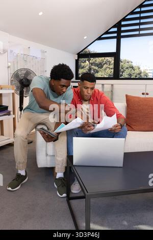 Collaboration de divers amis masculins examinant des documents dans une salle de style grenier, avec ordinateur portable et papiers Banque D'Images