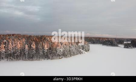 Forêt d'hiver illuminée par la lumière du coucher du soleil sur le lac gelé vue aérienne Banque D'Images