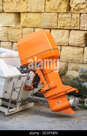 Gros plan d'un moteur hors-bord marin orange vif monté sur un petit bateau blanc à côté d'un mur de pierre. Banque D'Images