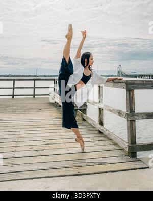 Ballerine effectuant une fente flexible sur la jetée au-dessus de l'eau Banque D'Images