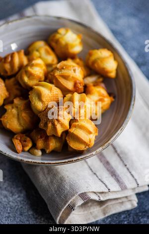 Une assiette de profiteroles au caramel fraîchement cuits au four se trouve sur une serviette rustique. Ces pâtisseries dorées et sucrées sont parfaites pour les amateurs de desserts, showcas Banque D'Images