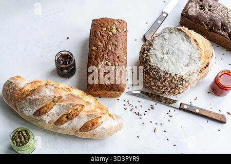 Vue de dessus d'une variété de pains au levain sains avec différentes graines, associés à des pots de pesto et de pâte de tomate sur une surface blanche, créant un aes Banque D'Images