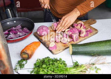 Une femme hache habilement les ingrédients sur une planche de bois tout en préparant un plat traditionnel équatorien. La scène capture l'essence vibrante du local Banque D'Images