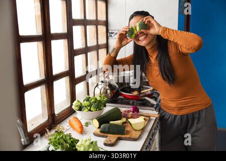Une femme prépare joyeusement un repas dans une cuisine équatorienne, en utilisant des légumes frais. La lumière du soleil coule à travers de grandes fenêtres, offrant un inviti chaleureux Banque D'Images
