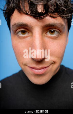 Gros plan d'un jeune homme avec un sourire charmant sur un fond bleu vif. L'expression attrayante et les couleurs vibrantes créent un engageant et moder Banque D'Images