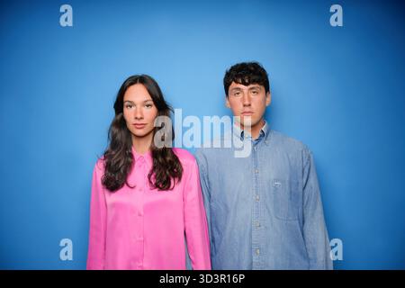 Un jeune homme et une jeune femme se tiennent côte à côte sur un fond bleu vif. Elle porte une blouse rose, tandis qu'il porte une chemise en denim, soulignant leur y Banque D'Images