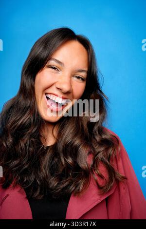 Portrait d'une femme joyeuse avec de longs cheveux ondulés profitant d'un moment de bonheur sur un fond bleu vif, véhiculant chaleur et positivité wi Banque D'Images