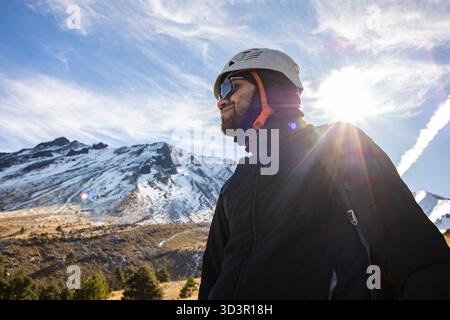 Un randonneur se tient en confiance dans l'équipement d'hiver, avec des montagnes glacées et un ciel lumineux en arrière-plan, mettant en valeur le frisson de la randonnée hivernale et alpine ex Banque D'Images