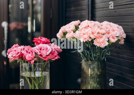 Élégants œillets roses et roses dans des vases en verre sont affichés dans un magasin de fleurs confortable, créant un arrangement floral charmant et esthétique qui rehausse Banque D'Images