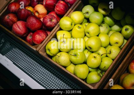 Un vif affichage de pommes biologiques fraîches dans un supermarché, avec une variété de pommes rouges et vertes juteuses soigneusement disposées dans des caisses en bois, showca Banque D'Images