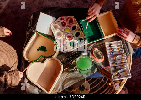 Enfants peignant des boîtes en bois avec des peintures colorées sur la table Banque D'Images