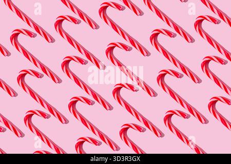Un motif festif de cannes de bonbon rouges et blanches disposées en diagonale sur un fond rose pastel. Les confiseries sucrées et rayées évoquent un Christ joyeux Banque D'Images