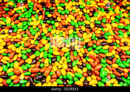 Une collection vibrante de dragées au chocolat enrobées de glaçures colorées. Le tableau multicolore présente des teintes vertes, oranges, marron et jaunes, créant un Banque D'Images