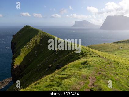 Vue imprenable sur les îles Féroé, avec ses falaises verdoyantes et son immense océan bleu sous un ciel lumineux. Terrain accidenté et îles lointaines com Banque D'Images