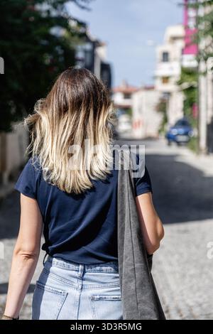 Une femme se promène le long des rues pavées pittoresques d'Alacati, Izmir, Turquie, profitant d'une journée ensoleillée, explorant la région charmante et dynamique. Banque D'Images