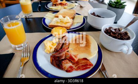 Un copieux petit déjeuner avec bacon croustillant, saucisses, œufs brouillés, crêpes, pain grillé avec fromage local et miel, céréales, pasteis de nata, et o frais Banque D'Images