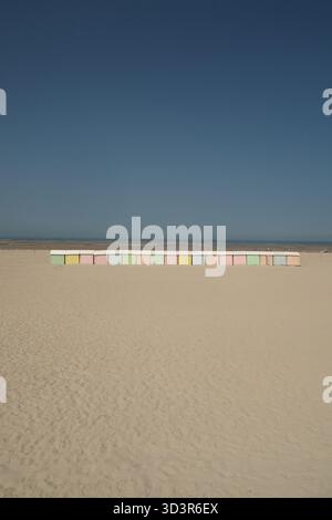 Une scène balnéaire sereine dans le nord de la France avec une rangée de cabanes de plage aux couleurs pastel sur un rivage de sable. Le ciel bleu tranquille rencontre l'horizon, creati Banque D'Images