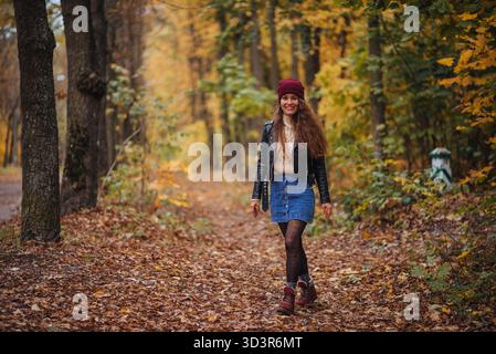 Une femme joyeuse en tenue d'automne se promène dans un parc coloré couvert de feuilles mortes. La scène capture l'essence du bonheur et de la tranquillité Banque D'Images