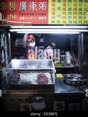Taipei, Taïwan - 20 mai 2023 : vue sur un étal cantonais animé de Congee, où un vendeur masqué dans un tablier rouge prépare des plats sous la grippe éclatante Banque D'Images