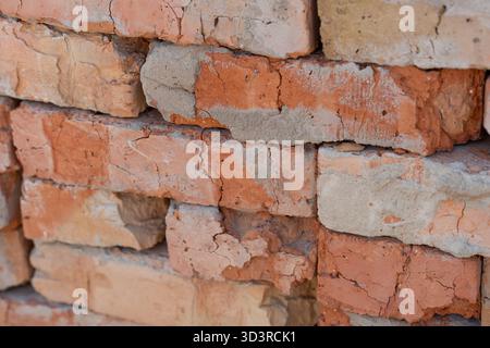 Des briques robustes dans des tons rouges et oranges variés forment une pile murale altérée. Les surfaces fissurées, le mortier exposé, la texture rugueuse transmettent la durabilité, l'histoire, l'esthétique de construction rustique Banque D'Images