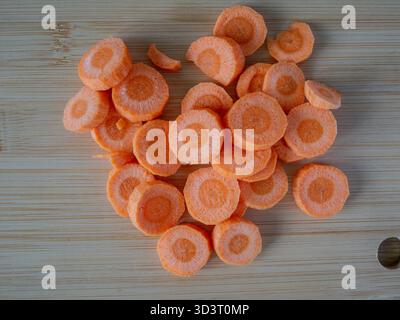 Tranches rondes de carotte fraîche sur une planche à découper en bois vue d'en haut. La mise en page épurée et la lumière naturelle mettent en évidence la texture et la couleur. Parfait pour Banque D'Images