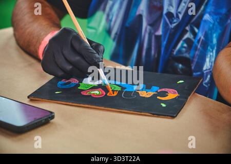 Lima, pérou. 01 novembre 2025 : personne portant un gant en utilisant un pinceau pour ajouter de la couleur aux lettres dessinées Banque D'Images