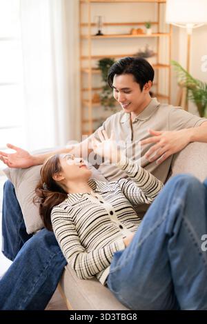 Couple adulte asiatique profite d'une conversation amoureuse détendue à la maison confortable sur le canapé partageant un moment intime tranquille dans leur salon moderne Banque D'Images