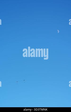Un grand plan d'un vaste ciel bleu clair mettant en scène trois individus engagés dans le parapente. Les petites silhouettes des parapentes avec leurs colorées Banque D'Images