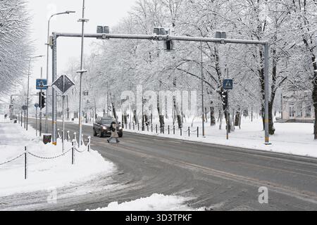 Un piéton traverse un passage pour piétons pendant une chute de neige à un feu vert. Une voiture s'est arrêtée pour laisser passer le piéton. La rue est Banque D'Images