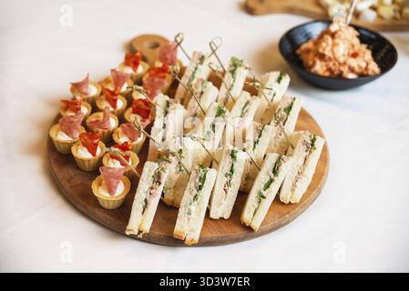 Nourriture, assortiment de sandwiches et canapés salés avec jambon et crème, magnifiquement disposés sur un plateau en bois pour un événement Banque D'Images