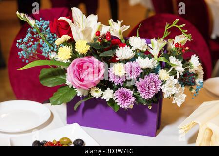 Nourriture, bouquet lumineux de fleurs mélangées avec des roses, des lis et des chrysanthèmes dans un récipient violet sur une table de banquet Banque D'Images